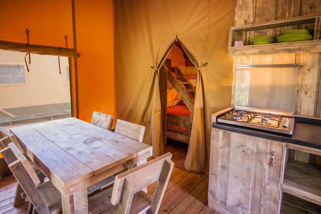 Intérieur d'une tente avec cuisine, table et lits superposés.