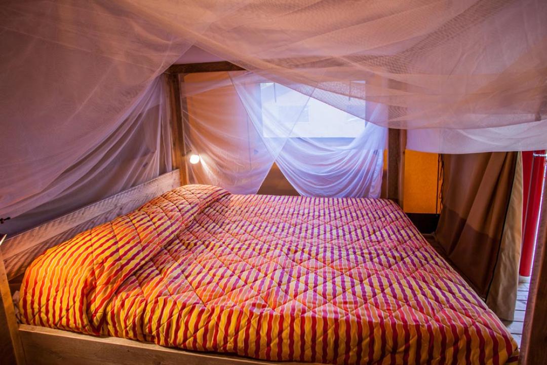 Double bed with mosquito net and colorful striped blanket.