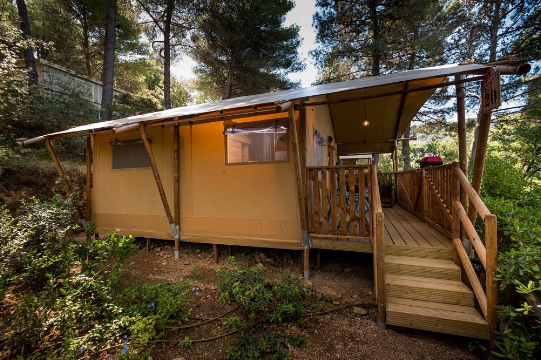 Holz-Glamping-Zelt in der Natur, mit Veranda und Zugangsramp.