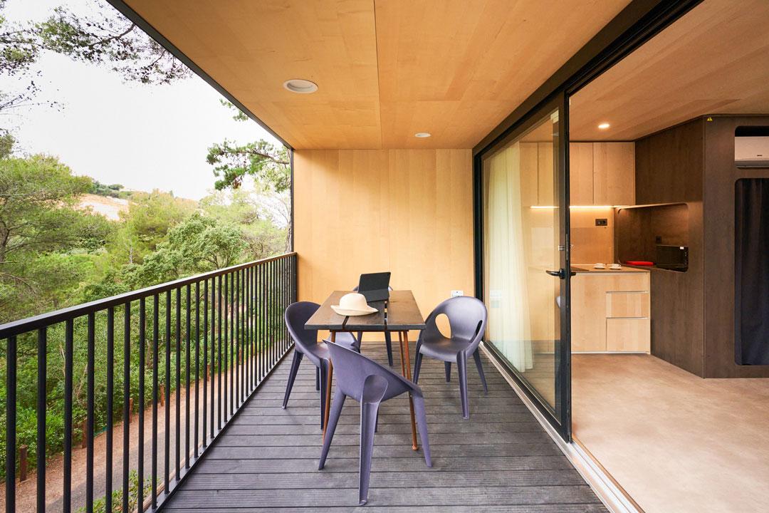 Modern balcony with table, chairs, and green view.