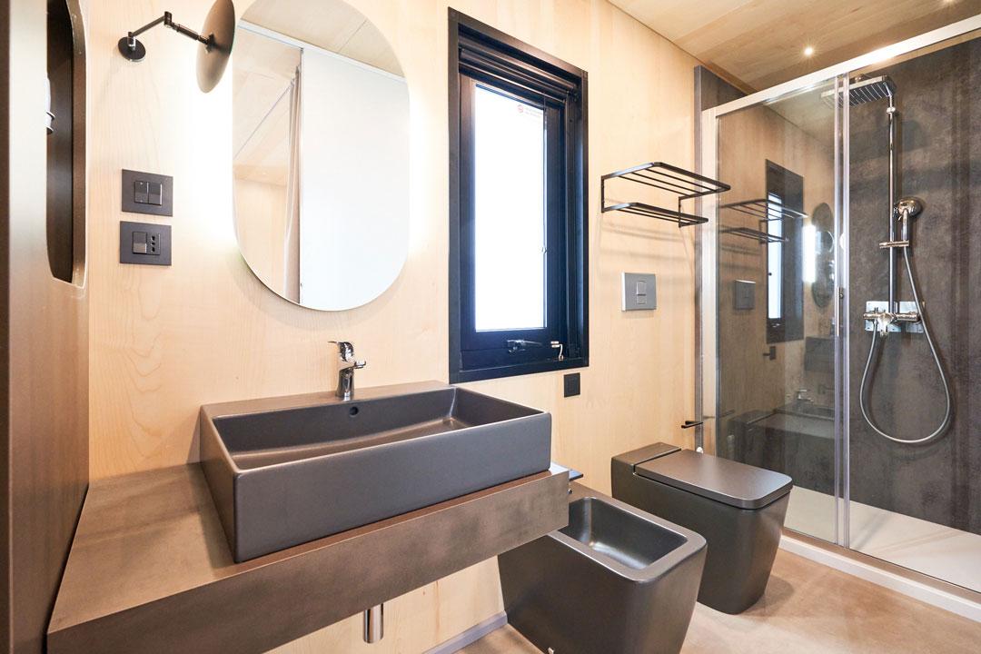 Nowoczesna łazienka z umywalką, lustrem, prysznicem i ciemnymi armaturami.