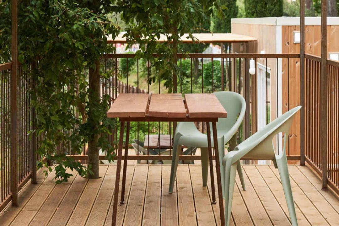 Terrasse avec table en bois, chaises et arbres environnants.