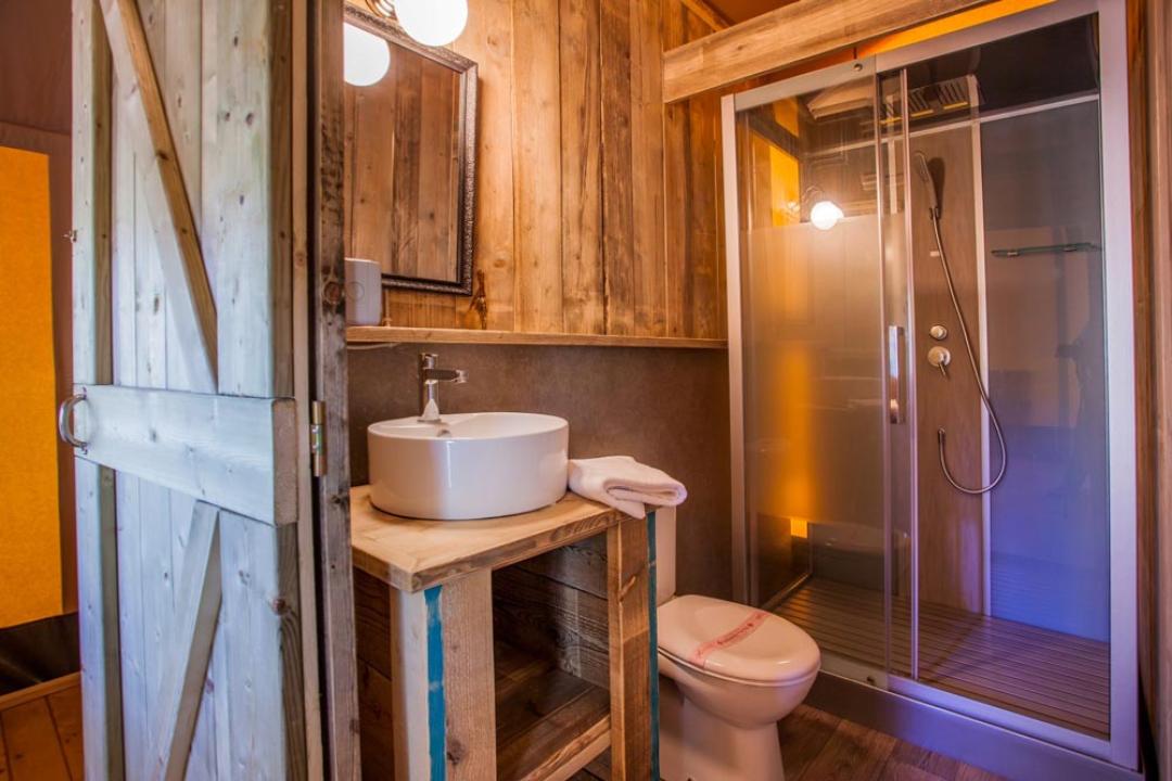 Rustykalna łazienka z prysznicem, umywalką i drewnianym lustrem.