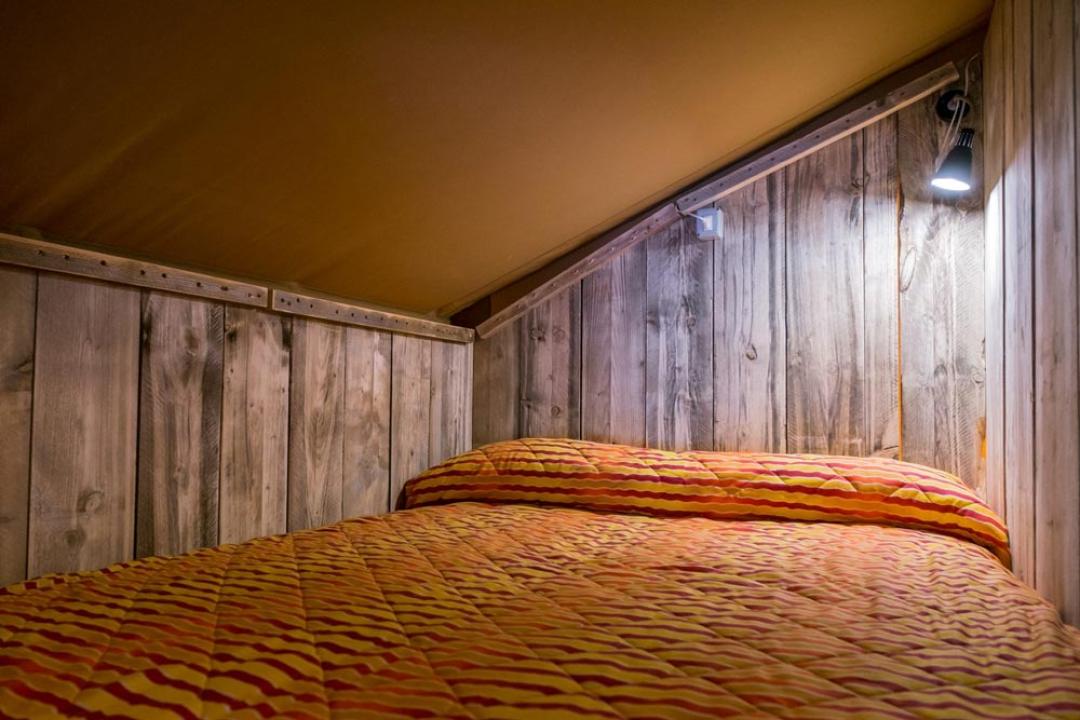 Łóżko na poddaszu z drewnianymi ścianami i miękkim oświetleniem.