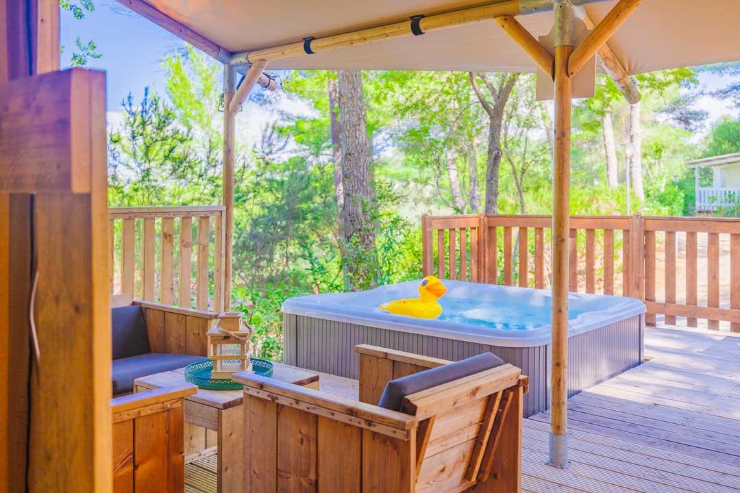 Terrasse avec jacuzzi et chaises en bois, entourée de nature.
