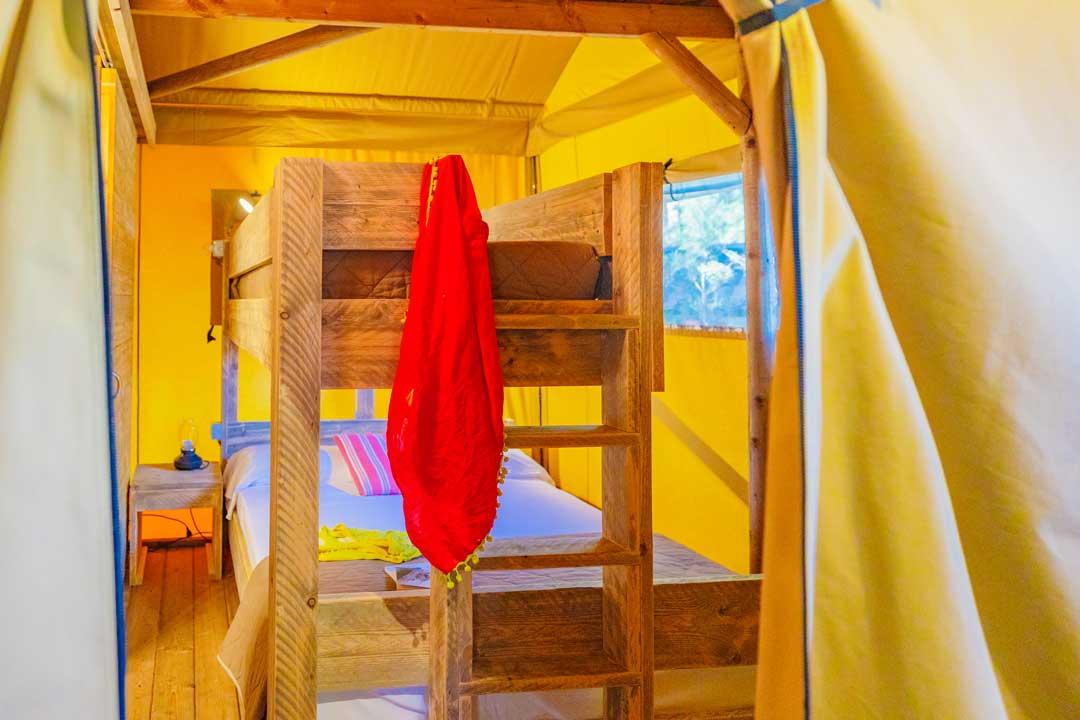 Łóżko piętrowe w żółtym namiocie z wiszącą czerwoną tkaniną.
