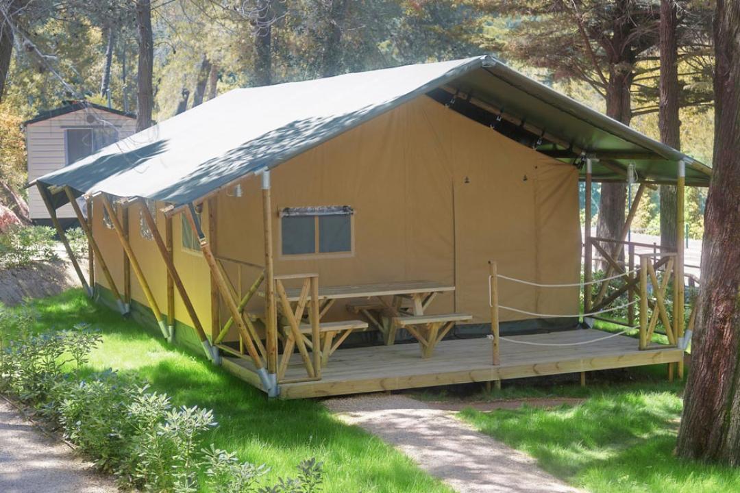 Glamping-Zelt auf einem Campingplatz mit Veranda und Picknicktisch.