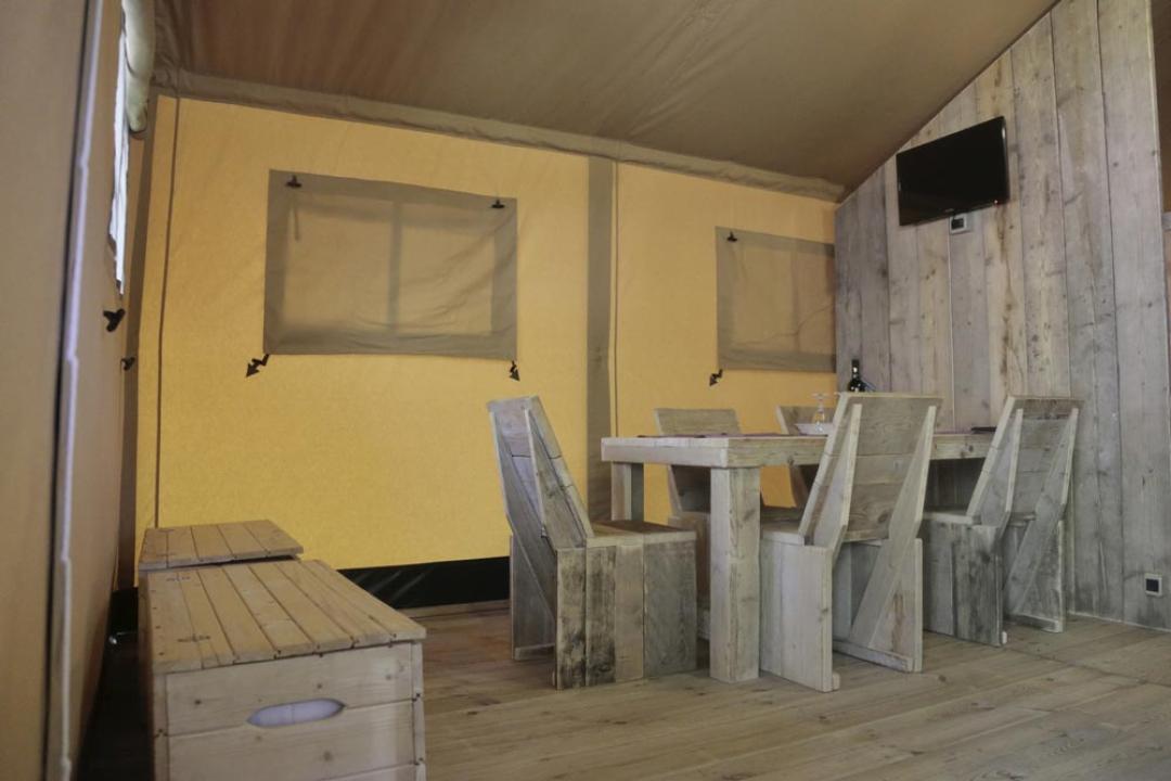 Wnętrze namiotu z drewnianym stołem i krzesłami, telewizor na ścianie.